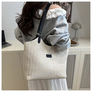 Detail of a woven straw tote bag with black leather straps and fashion label on a model