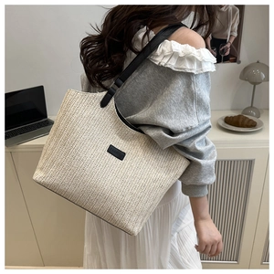 Detail of herringbone weave straw tote bag with black leather straps and fashion label