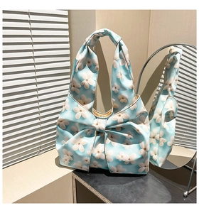 Detail of light blue hobo bag with white floral print and decorative bow on the front side