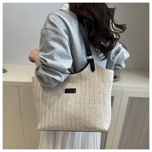 Détail du sac cabas en paille tressée avec anses en cuir noir et écusson tendance