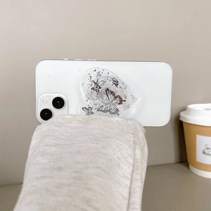 Close-up of heart-shaped phone grip with butterfly sequins and glitter on white phone