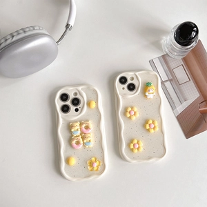 Detail of cream wave-edge iPhone cases with glitter, resin bear, and flower charms