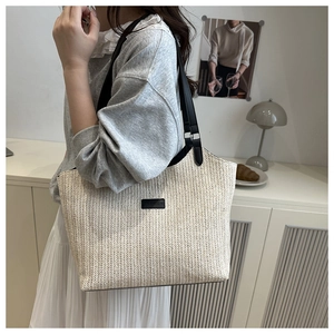 Close-up of woven straw tote bag featuring black leather FASHION label and straps