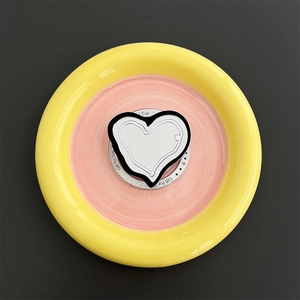 Macro view of MagSafe phone holder with heart-shaped mirror on a colorful ceramic plate