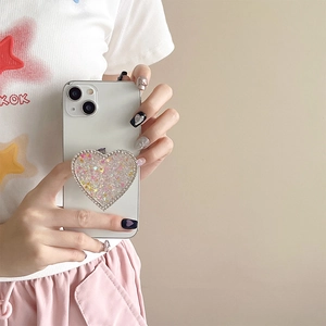 Close-up of a heart-shaped glitter phone grip with rhinestones held by a person