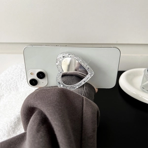 Detail of a heart-shaped glitter phone socket with a built-in makeup mirror on white phone