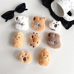 Cute plush capybara and potato phone grip holders arranged on a minimalist white surface