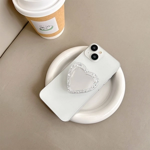 Detail of silver glitter heart-shaped phone grip and mirror on white smartphone