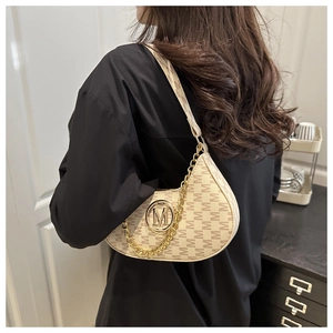 Close-up of beige crescent underarm bag featuring monogram pattern and gold metal logo