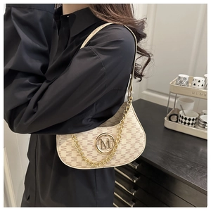 Detail of beige crescent underarm bag with letter print and gold chain on model