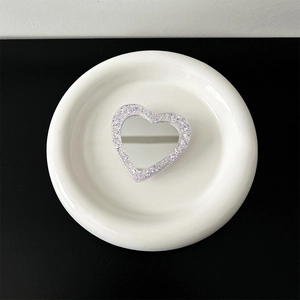 Macro detail of heart-shaped glitter phone grip with purple sparkles on white ceramic tray