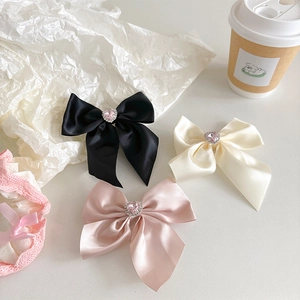 Detail of satin bow phone grips in black, cream, and pink with heart rhinestone centers