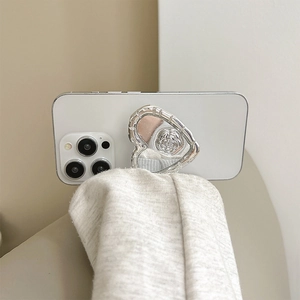 Close-up of silver heart-shaped phone socket grip with rose relief on white phone.