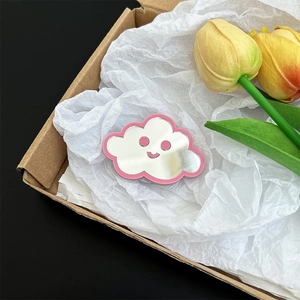 Close-up of a cute pink cloud-shaped mirror phone grip with a smiley face in a box
