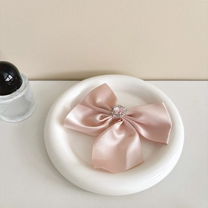 Detail of pink satin bow hair clip with heart-shaped gemstone and crystal embellishment