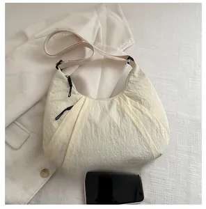 Détails du sac demi-lune en nylon crème montrant le tissu texturé et la bandoulière