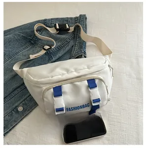 Detail view of white canvas crossbody bag with blue buckle strap and phone for size reference