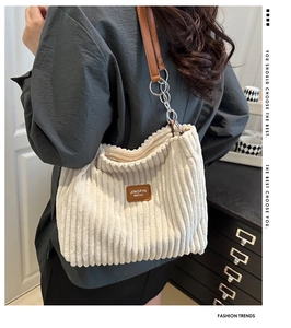Close-up of cream corduroy tote bag featuring brown leather strap and chain detail