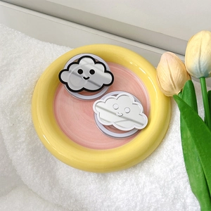 Detail of cloud-shaped phone grips with mirrors and smile faces on a ceramic tray