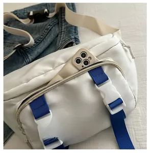 Detail of white crossbody bag featuring blue nylon strap and plastic buckle on denim