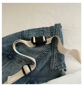 Detail of adjustable cream fabric shoulder strap and buckle on blue denim crossbody bag