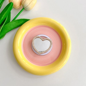 Macro view of heart-shaped rhinestone phone grip mirror with gold base on a floral tray