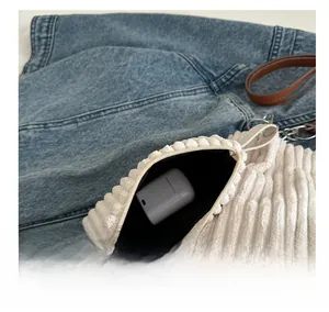 Close-up of white corduroy mini pouch with silver zipper for earphones on denim background