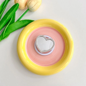 Detail shot of heart-shaped rhinestone phone mirror grip on a decorative ceramic plate
