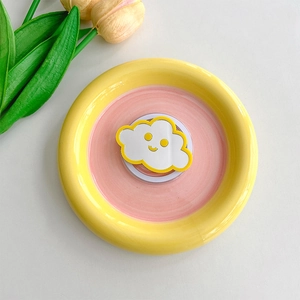 Close-up of cloud-shaped phone grip with smiling face inside a pastel ceramic tray