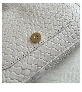 Detail of golden magnetic clasp and woven texture on the white leather shoulder bag