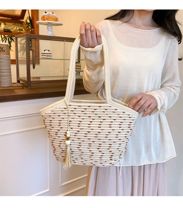 Detail of woven straw tote bag featuring white tassels and decorative wooden beads