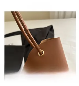 Detalle de bolso tote de cuero marrón con ojales metálicos y correas finas