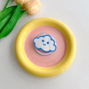 Detail of cloud-shaped makeup mirror phone grip on a yellow ceramic tray with tulips