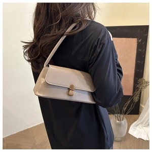 Detail van een beige lakleren baguette tas met gouden gesp gedragen door een model