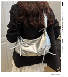 Detail of a silver metallic bow shoulder bag styled on a model with a pleated strap design