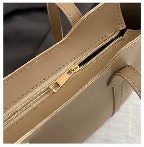 Close-up of smooth golden metal zipper on beige leather tote bag with fine stitching