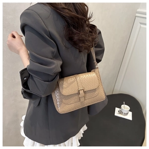 Detail view of beige crocodile embossed underarm bag with decorative metal buckle clasp