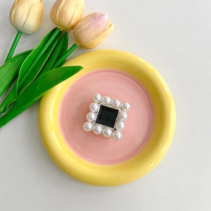 Detail of square black enamel phone stand surrounded by glossy white pearls on a tray
