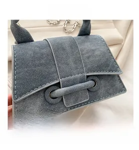 Detail of grey-blue denim crossbody bag featuring a unique knot clasp and metal chain strap