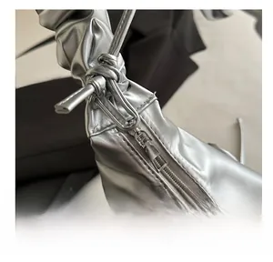 Detail of metallic silver bag showing smooth metal zipper and pleated knot handle texture
