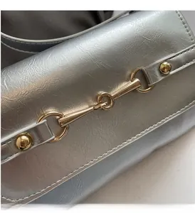 Detail of silver metallic leather handbag featuring a golden horsebit buckle and fine stitching
