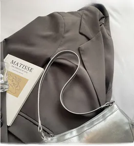 Detail einer silbernen Metallic-Schultertasche mit glänzender Textur auf dunklem Sakko
