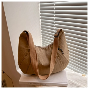 Détail du sac demi-lune plissé kaki foncé avec bandoulière sur un livre blanc en décor
