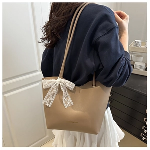 Vista detallada del bolso tote caqui con lazo de encaje blanco y tipografía de moda
