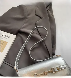 Detail of silver faux leather shoulder bag with gold horsebit buckle on suit background