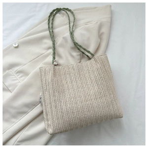 Détail de la texture du sac cabas en paille avec anses vertes sur une veste blanche