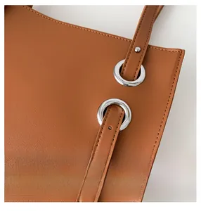 Detail of silver metal eyelets and adjustable strap on a brown leather tote bag