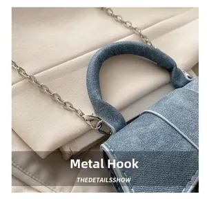Detail of silver metal hook and white stitching on a light blue denim handbag