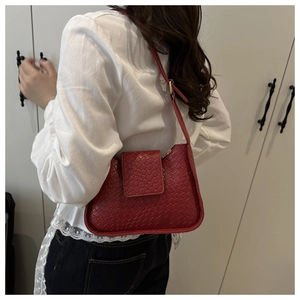 Détail du sac à bandoulière rouge foncé avec texture croco et boucle dorée sur le côté