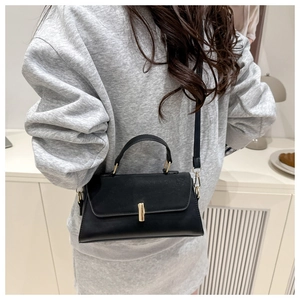 Detail of a black leather handbag featuring a golden rectangular clasp and top handle